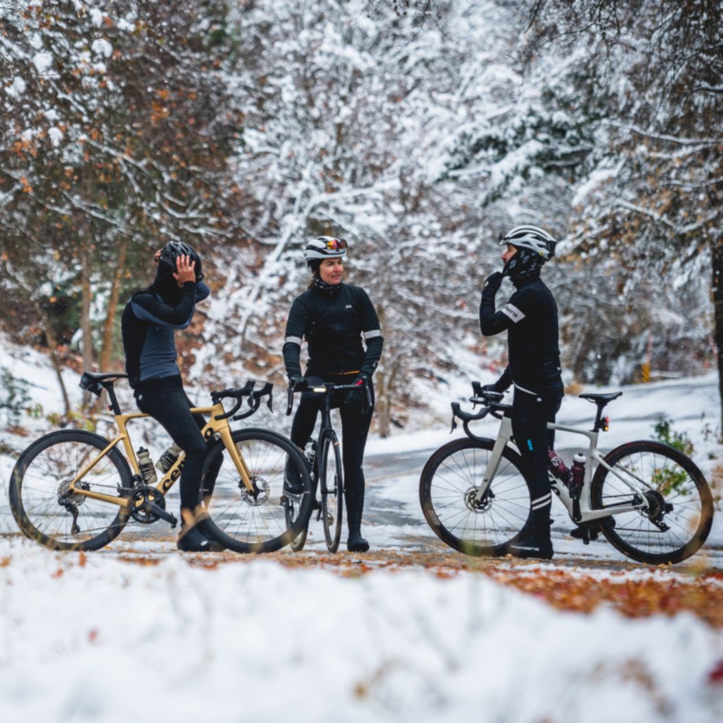 Three road cyclists stand over their bikes in the road for a chat on a very snow day.